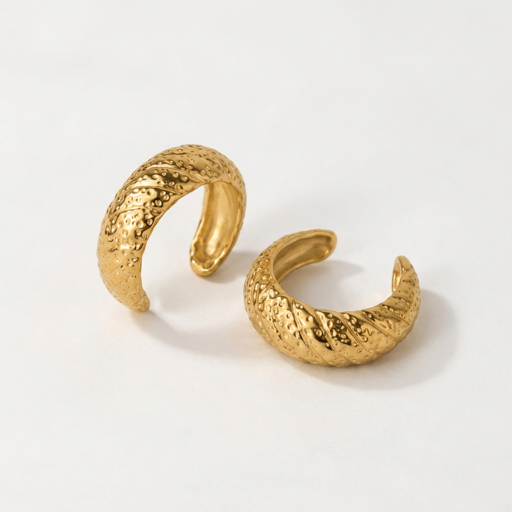 Anel NERA dourado em aço inoxidável, de formato aberto e textura em relevo — fotografia de produto.
