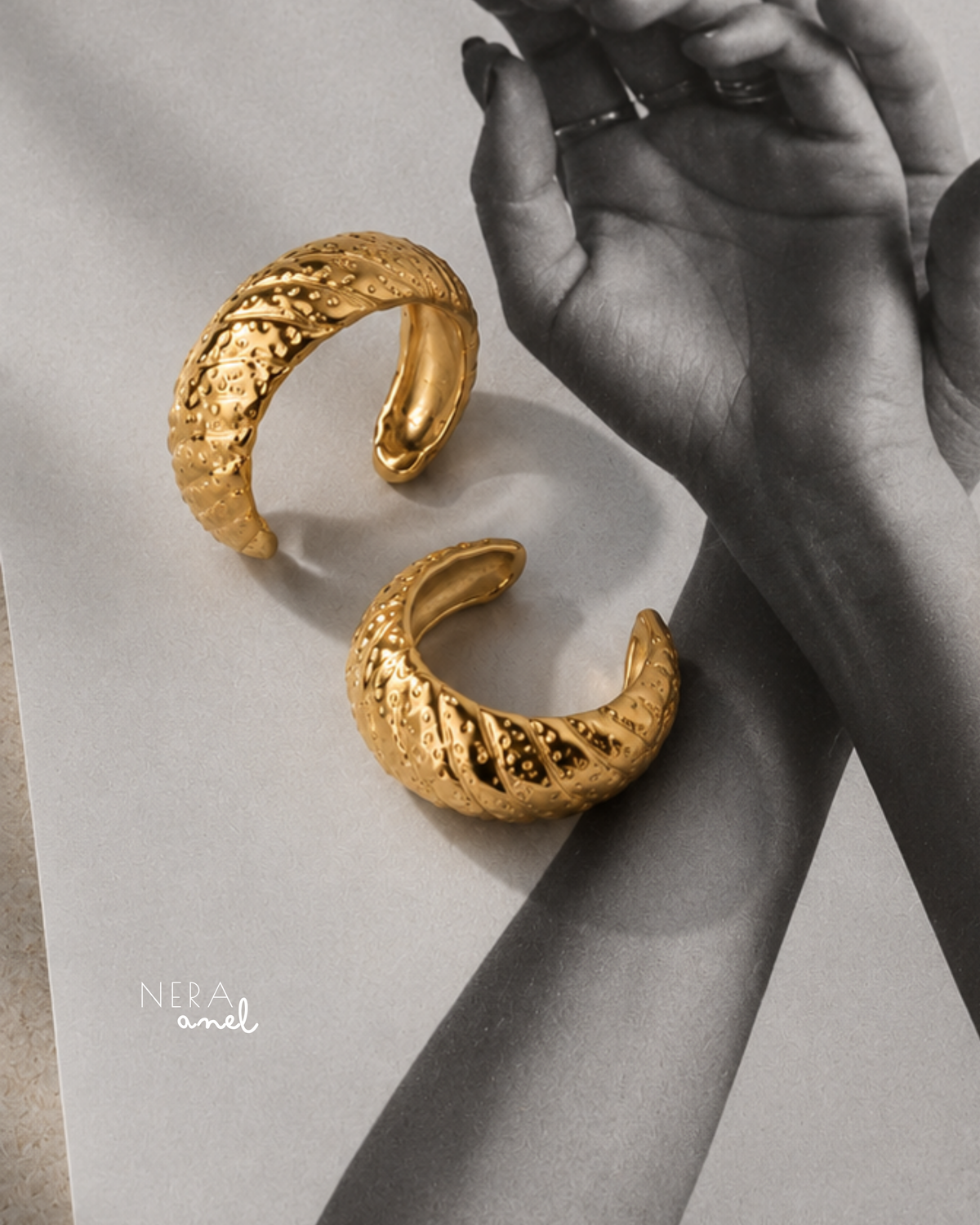 Anel NERA dourado em aço inoxidável visto de outro ângulo, destacando as linhas diagonais e o relevo texturizado.