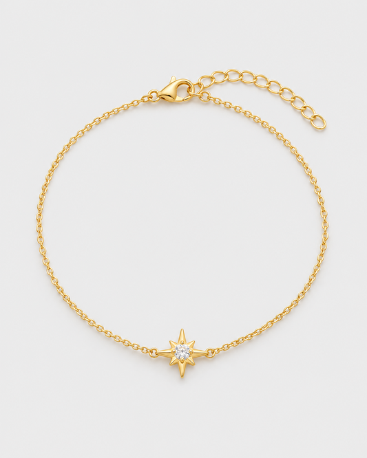 Pulseira ASTRA dourada em aço inoxidável, disposta em círculo com estrela central e zircónia, sobre fundo cinzento claro
