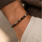 Pulseira masculina ATLAS com pequenas contas de pedras naturais facetadas no pulso de um homem com malha castanha